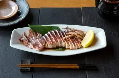 Grilled squid rings on white plate with lemon, sauce, and chopsticks.