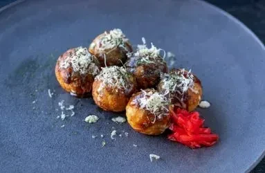 Six Takoyaki with dark sauce, white flakes, and red ginger.