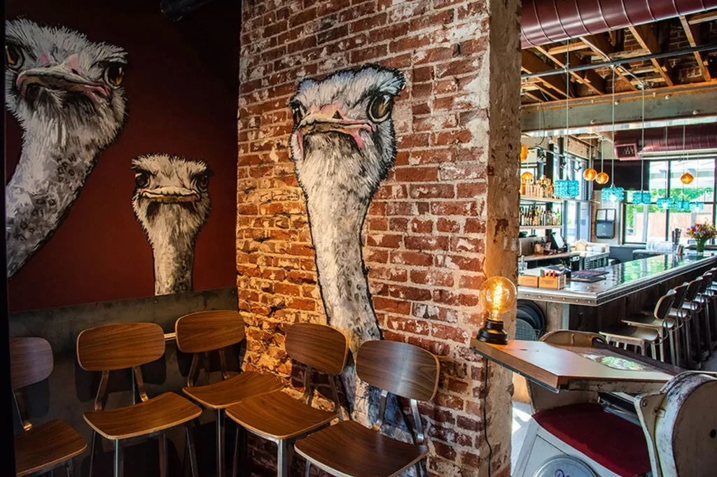 Quirky industrial restaurant interior with ostrich head murals and a bar.