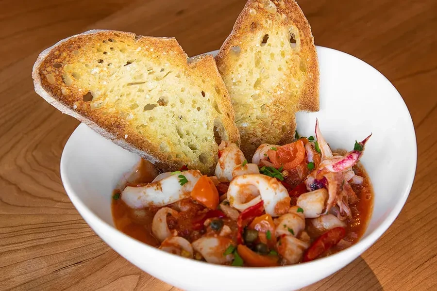 Calamari in tomato sauce with bread, cherry tomatoes, capers, herbs.