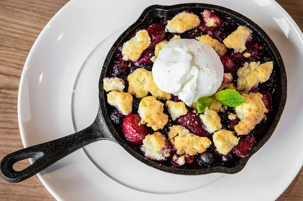 Close-up skillet berry cobbler with vanilla ice cream and a mint sprig.