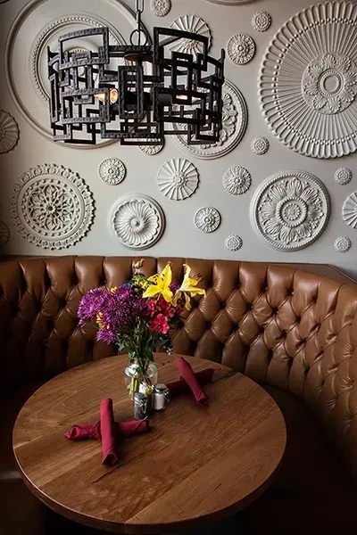 Restaurant booth with tufted brown leather, flowers, and ornate wall.