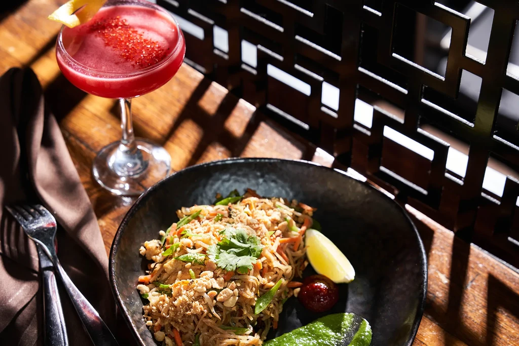 Noodle dish with peanuts, cilantro, lime, and red cocktail.