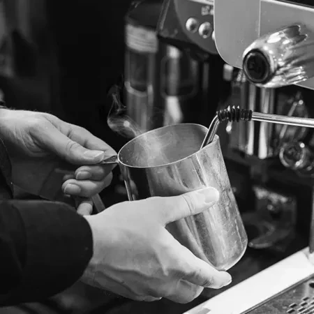 Black and white close-up: Hands steaming milk using an espresso machine.
