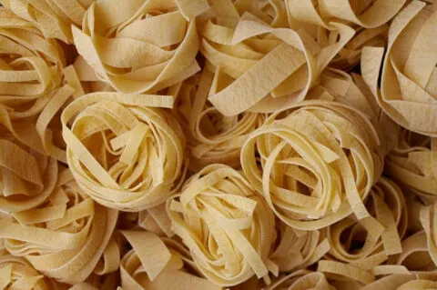 Uniform pattern of raw, coiled dried pasta nests.