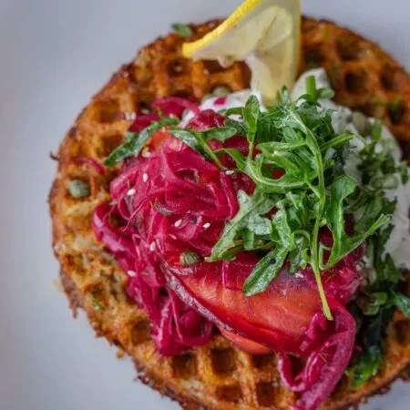 Golden savory waffle with red cabbage, green arugula, white sauce, lemon.