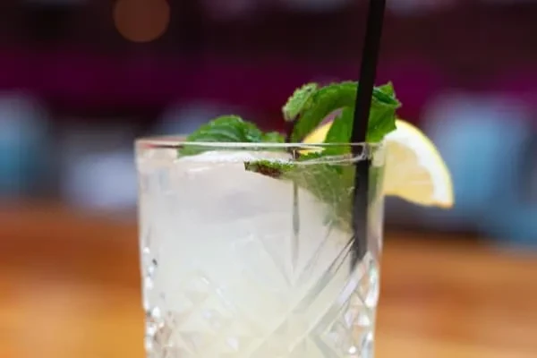 Textured glass with iced lemonade, mint leaves, lemon, and black straw.