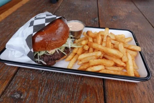Burger and fries with sauce on a tray on a wood table.