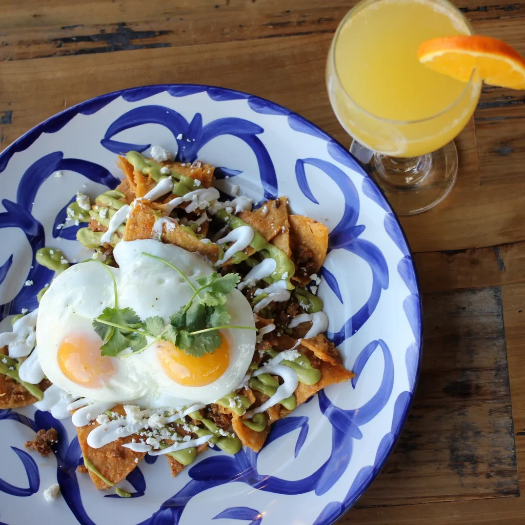 Chilaquiles with fried eggs, sauces, cheese, and an orange mimosa.