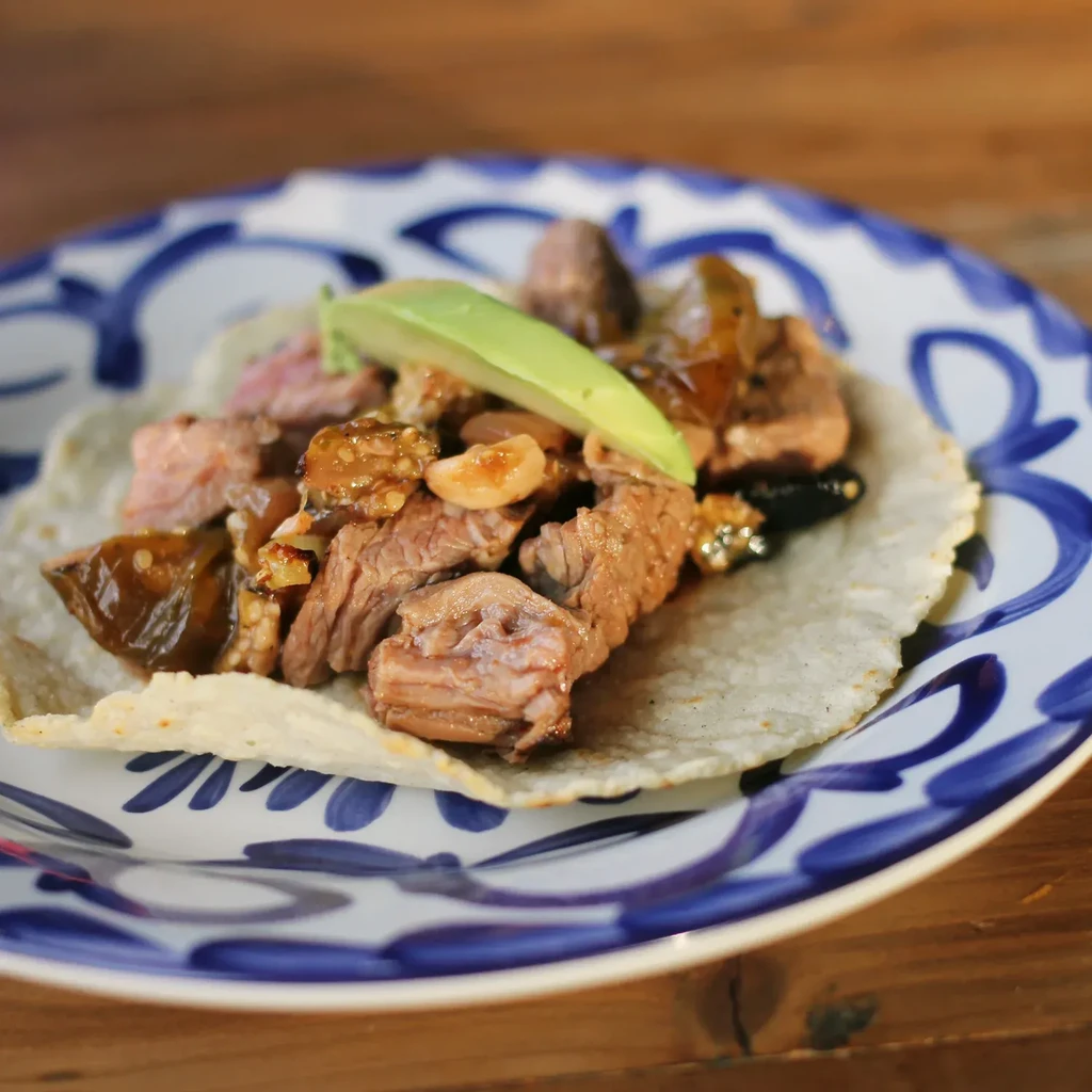 Close-up of a meat taco with avocado on a blue-patterned ceramic plate.