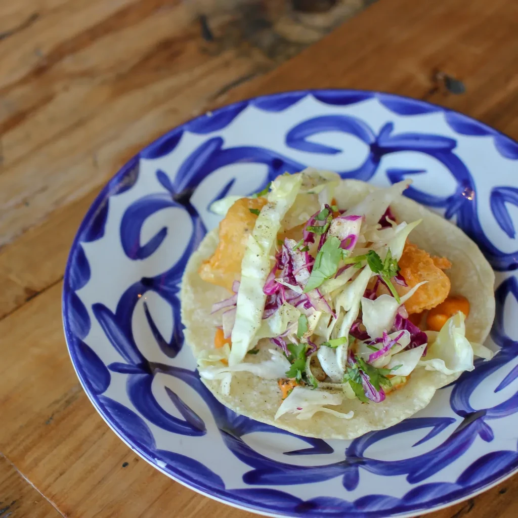 Single taco with battered protein and cabbage on a blue patterned plate.