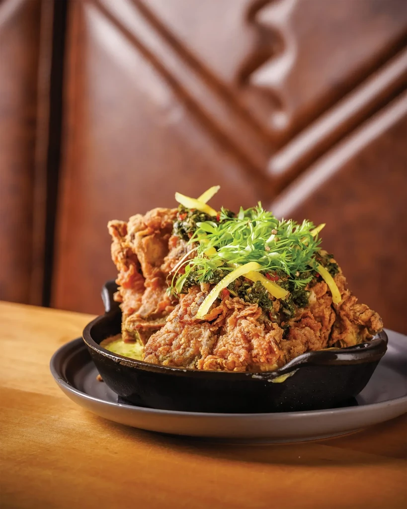 Crispy fried chicken topped with microgreens and lemon zest in a dark bowl.
