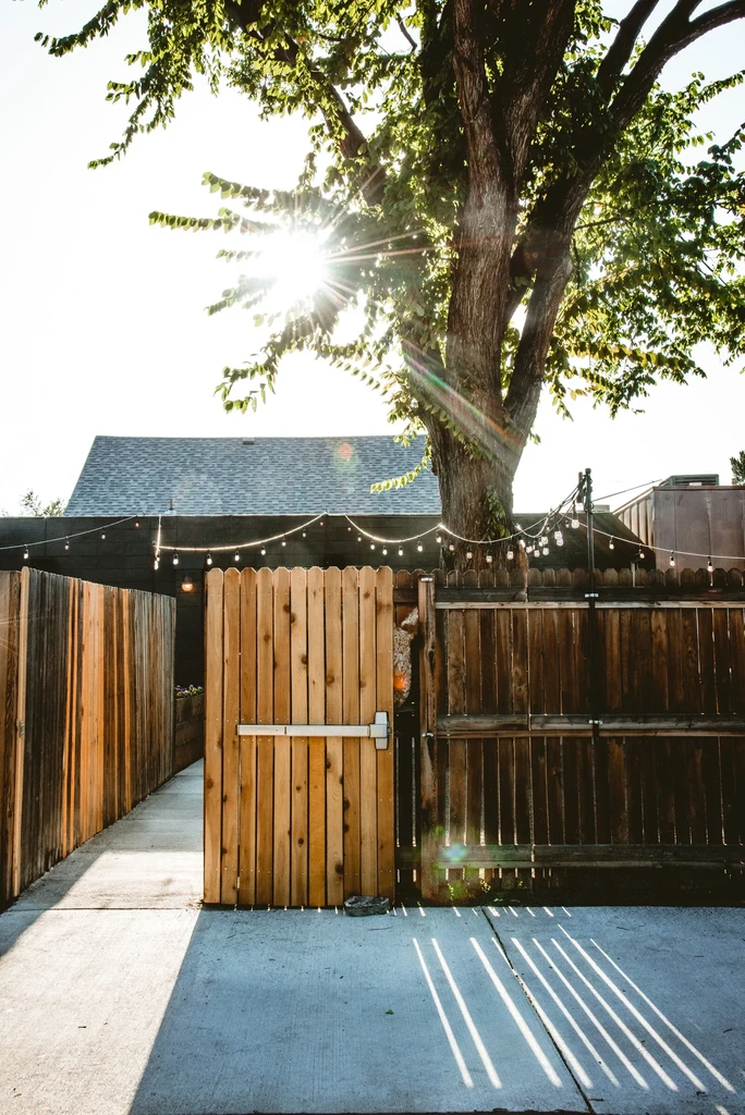 Sunlit outdoor pathway through a rustic wooden gate with string lights.