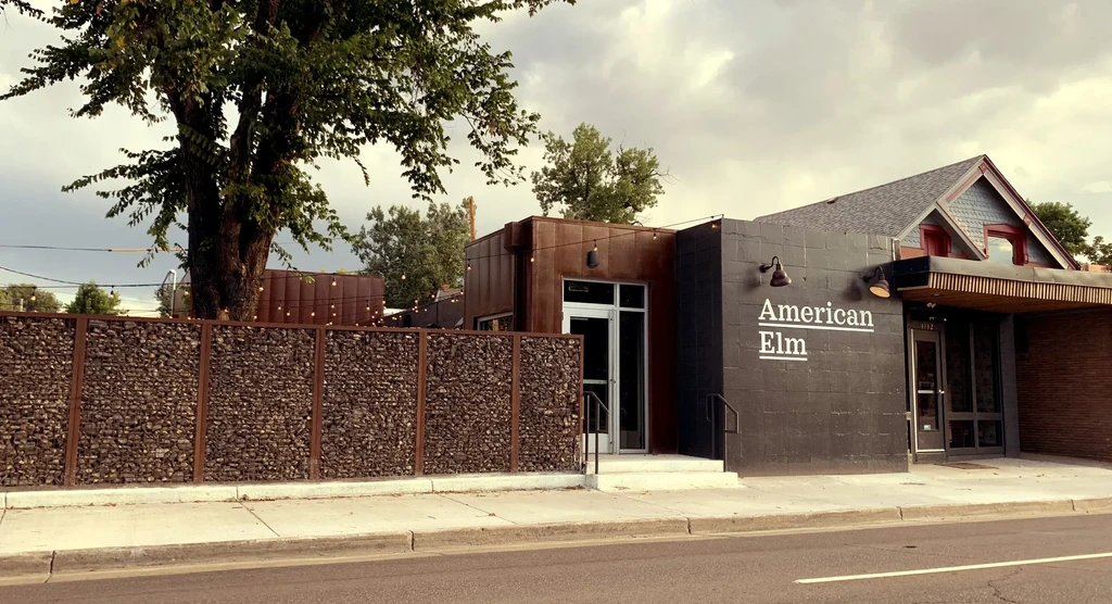 Exterior of American Elm building with gabion wall, patio, and tree.