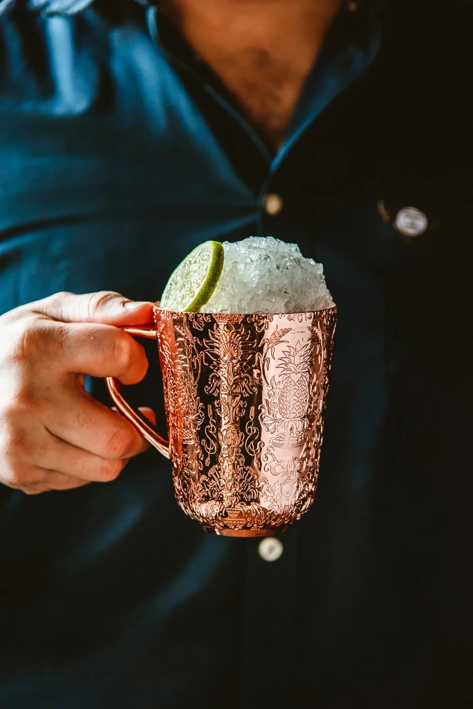 Hand holds ornate copper mug with drink, crushed ice, and lime.