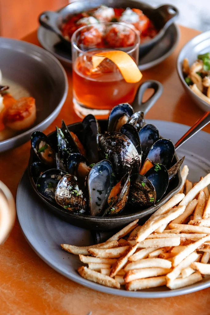 Mussels, golden fries, and an amber cocktail on a warm table.