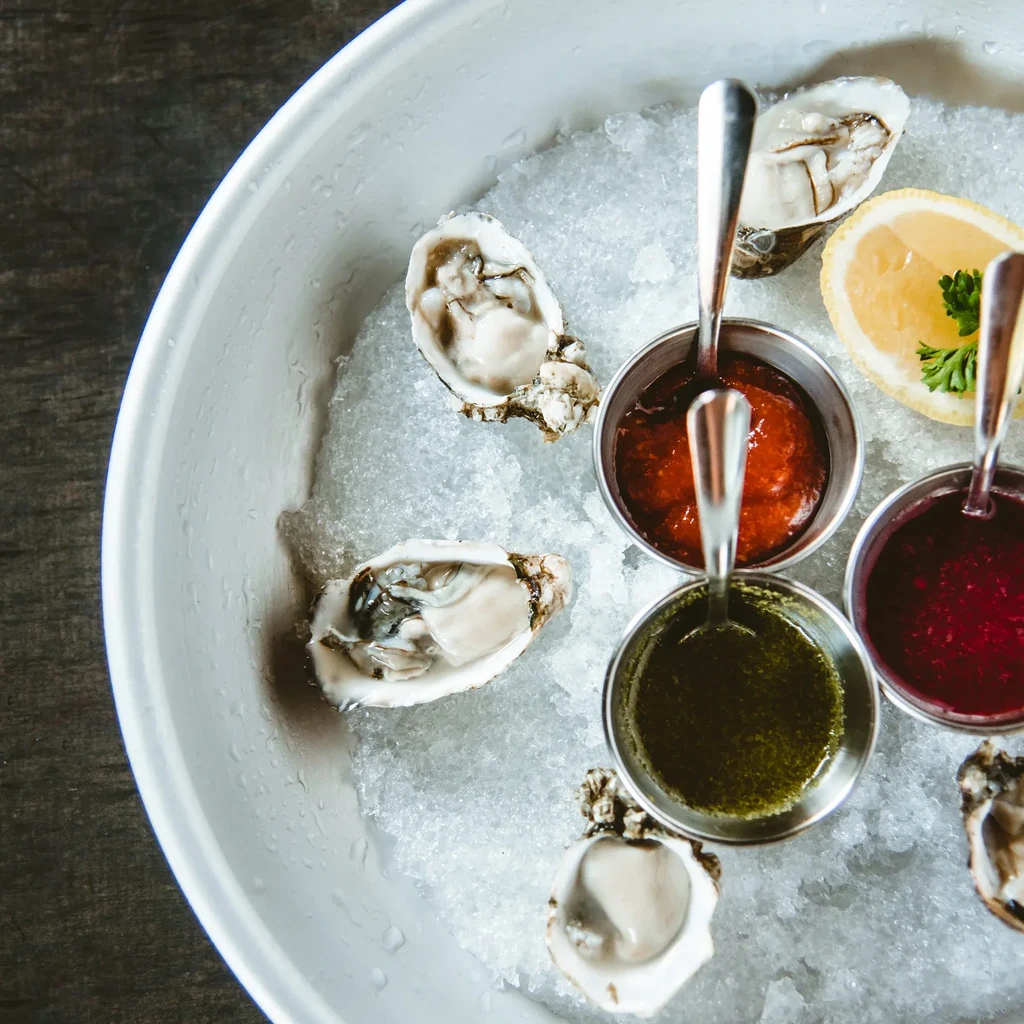 Fresh shucked oysters on ice with three sauces and lemon wedge.