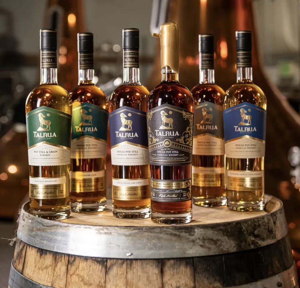 Six Talrua Distillery whiskeys, one gold-sealed, on a barrel at a distillery.