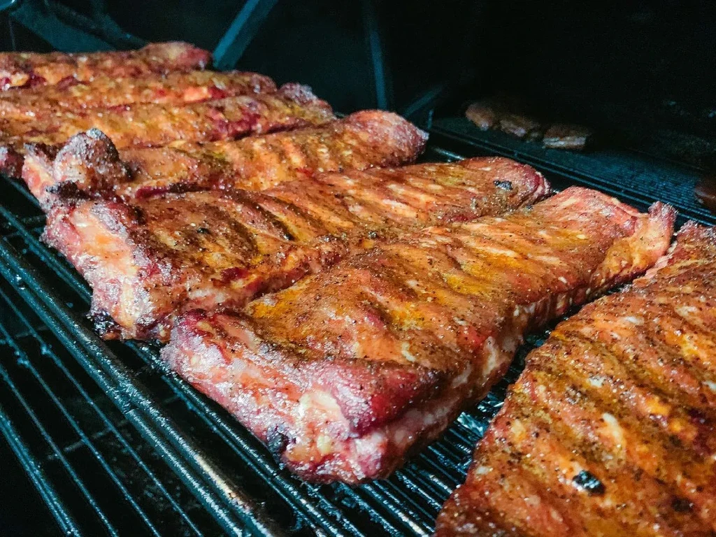 Multiple racks of seasoned ribs on a grate inside a smoker.