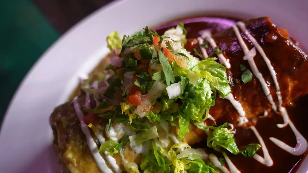 Enchiladas with red and green sauces, white crema, and fresh toppings.