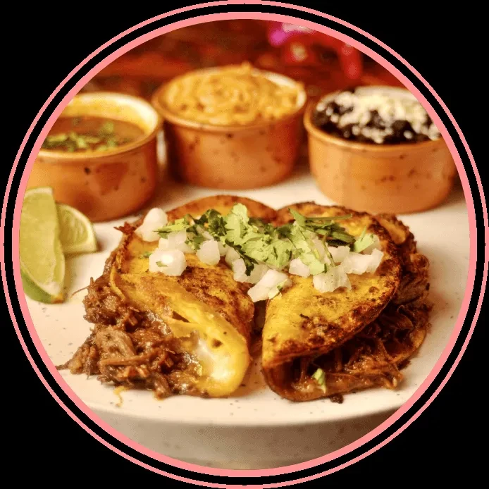 Plate with two birria tacos, consommé, beans, and lime wedges.