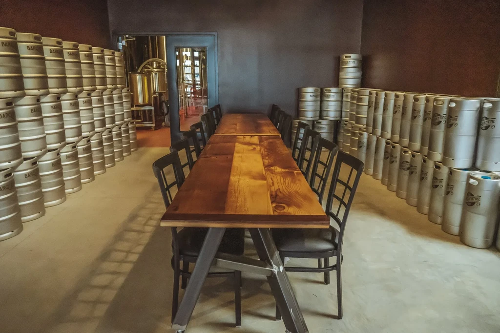 Rustic table and chairs in a brewery event room with stacked kegs.