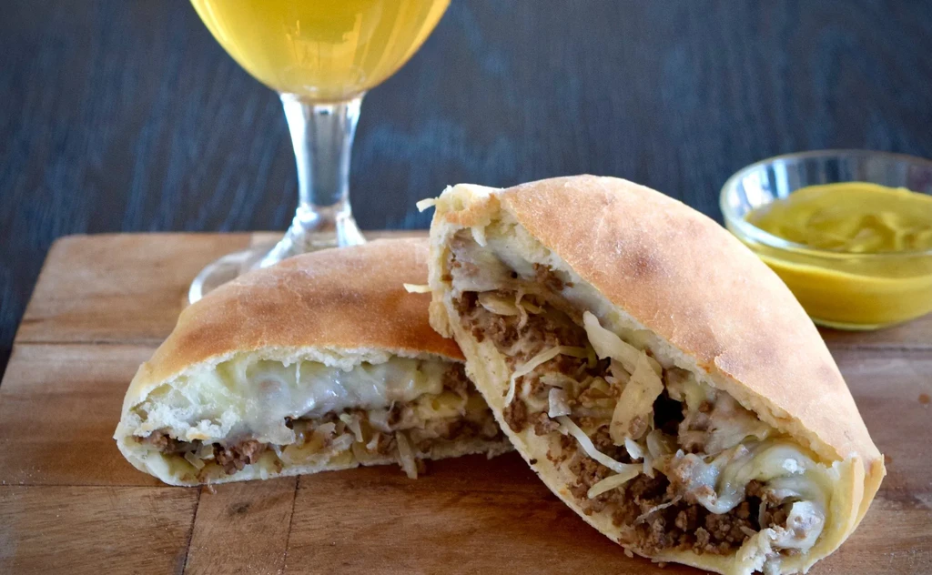 Pastry cut open, showing meat, cheese, cabbage filling, with beer and dip.