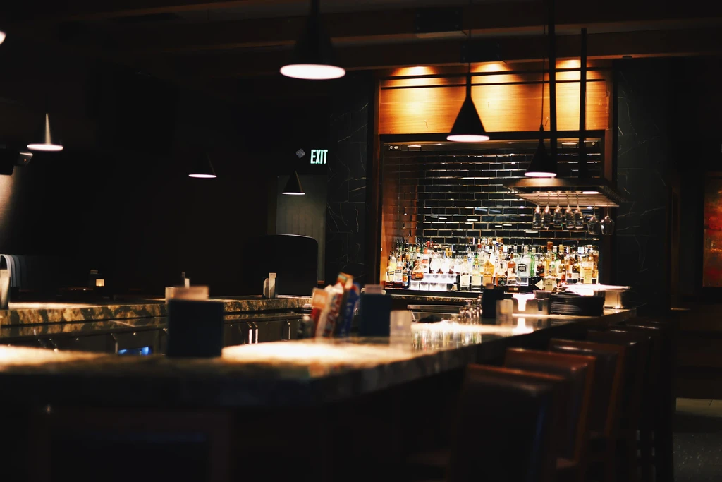 Dimly lit, upscale bar with glowing bottles, polished counter, and stools.