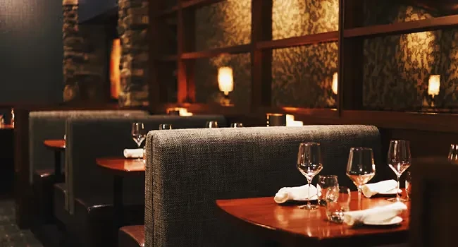 Dimly lit restaurant interior with a set table, wine glasses, and dark booths.