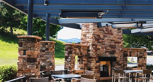 Empty patio with stone fireplace, modern pergola, heaters, and mountain views.