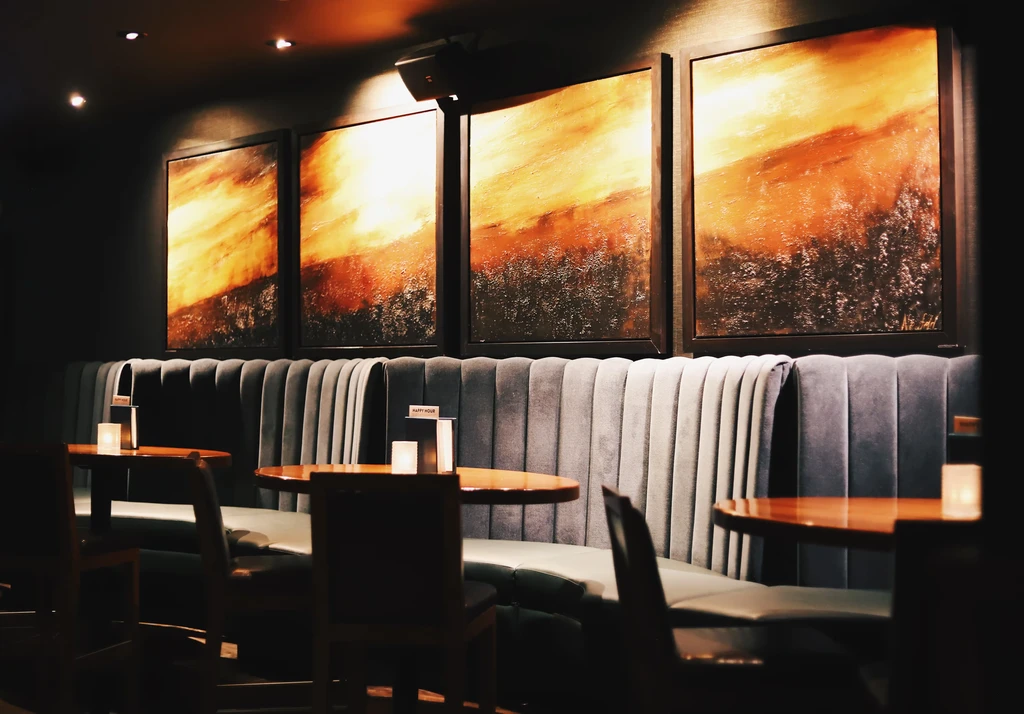 Restaurant interior with a velvet booth, abstract art, and candlelit tables.