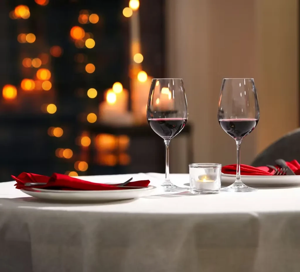 Table setting with two red wine glasses, candle, and blurred lights.