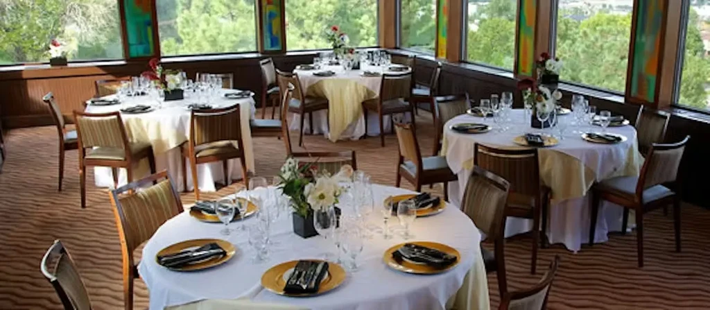 Formal restaurant dining room with set tables and a panoramic view.