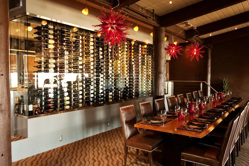 Restaurant interior: glass wine wall, set table, red chandeliers.