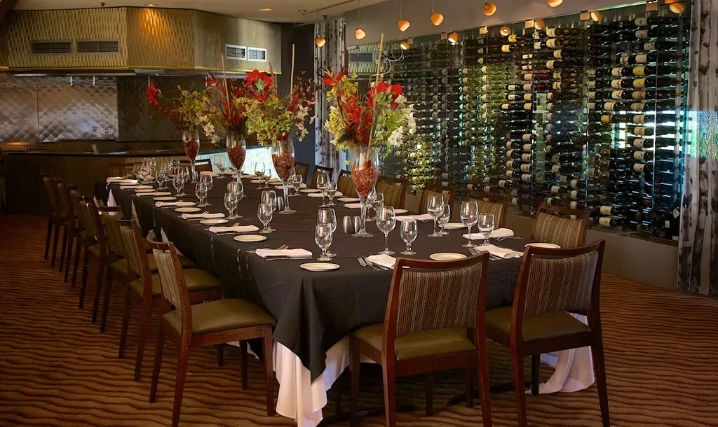 Upscale private dining table, floral centerpieces, visible kitchen, and wine wall.