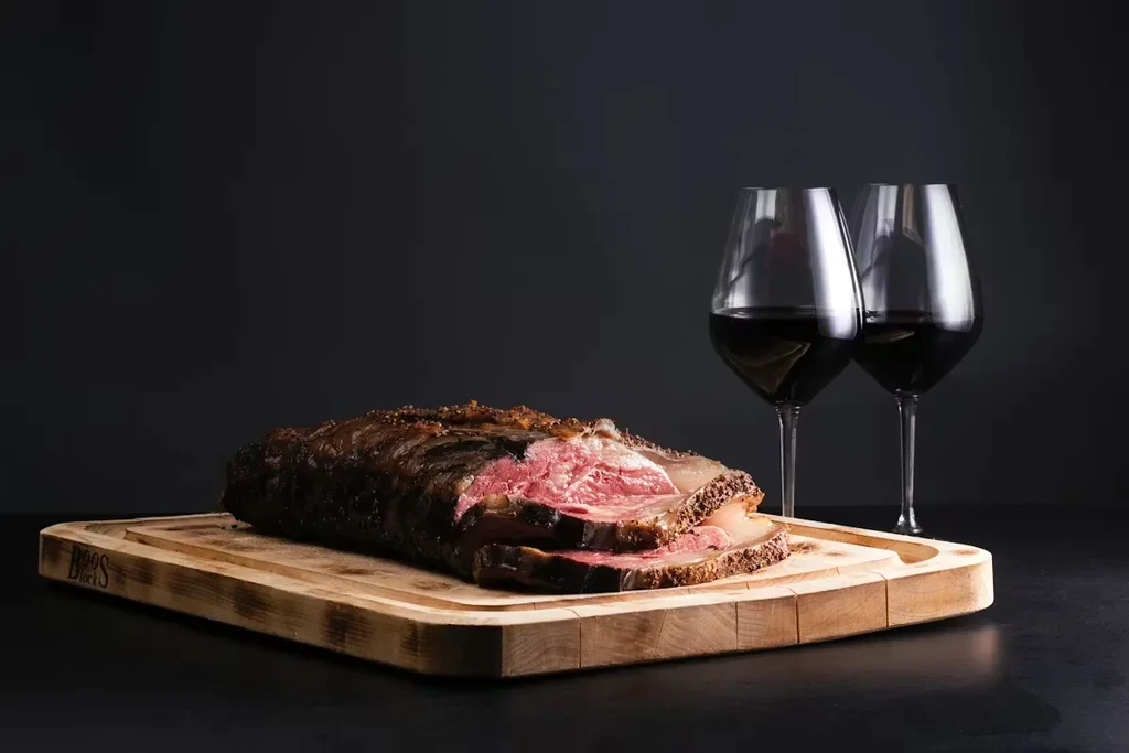 Sliced, medium-rare roasted meat on a wooden board with red wine.