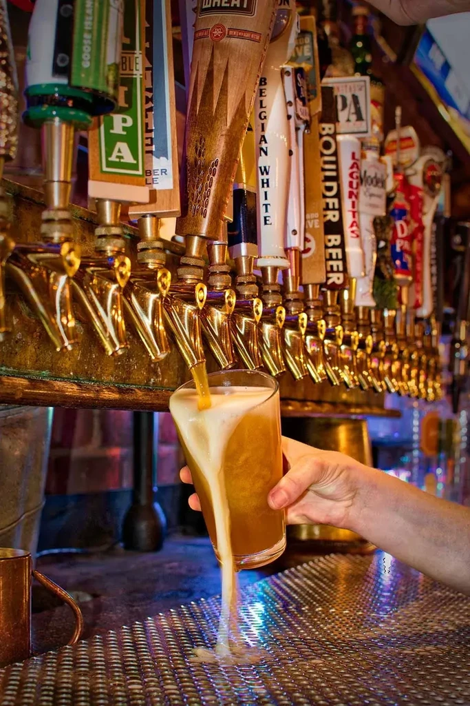 Overflowing amber beer glass below many branded bar taps.