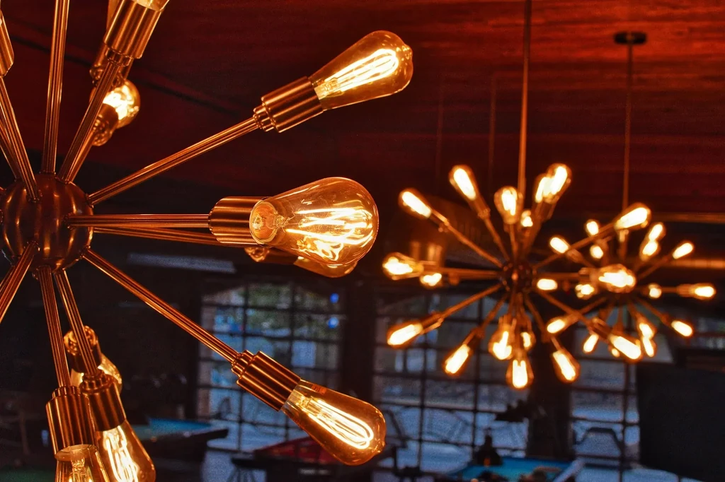 Sputnik chandelier with glowing Edison bulbs, blurred lounge background.