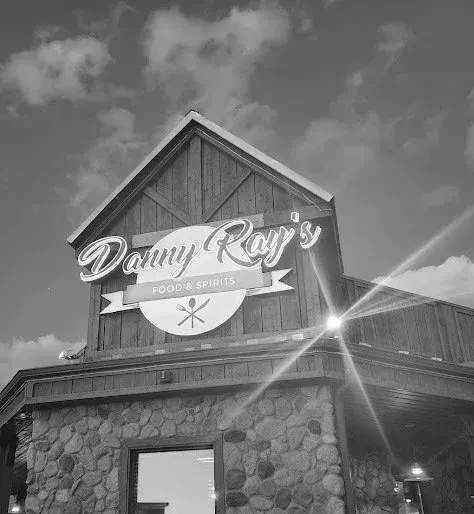 Monochrome exterior of rustic Danny Ray's Food & Spirits with illuminated sign.