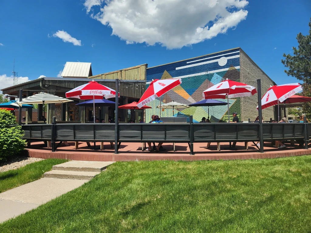 Sunny outdoor patio restaurant with Coca-Cola umbrellas and geometric mural.