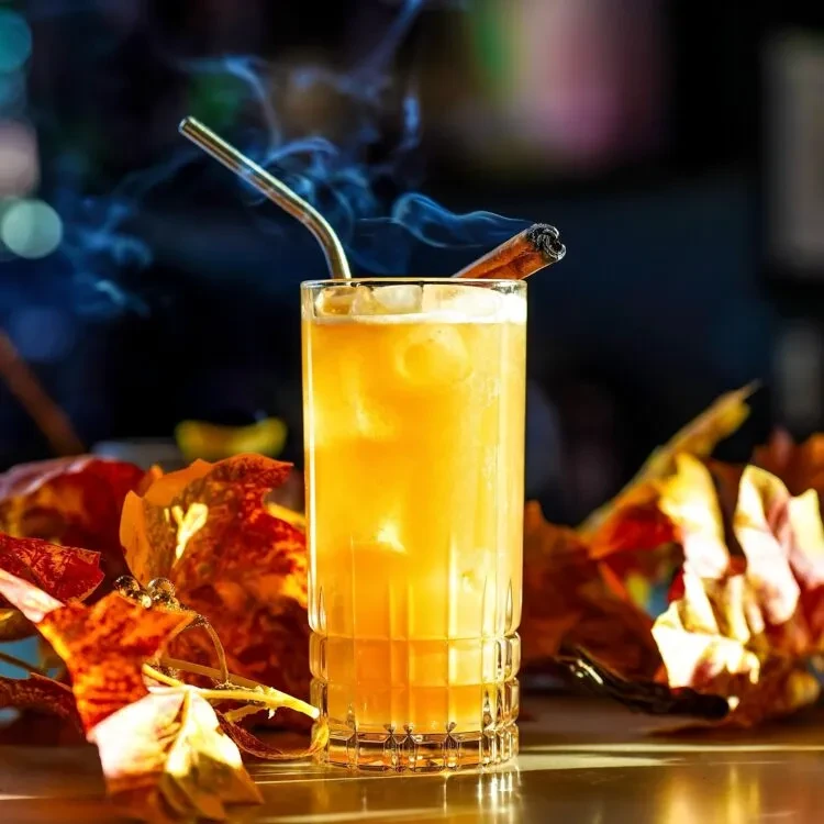 Amber cocktail in textured glass with smoking cinnamon and autumn leaves.