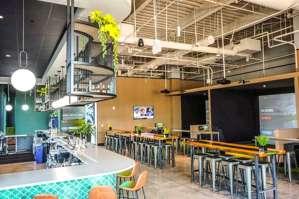 Industrial-chic bar with teal tiles and golf simulator bays.