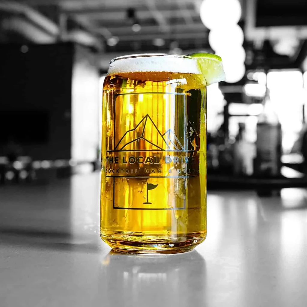 Golden cocktail in can-shaped glass with lime and The Local Drive logo.