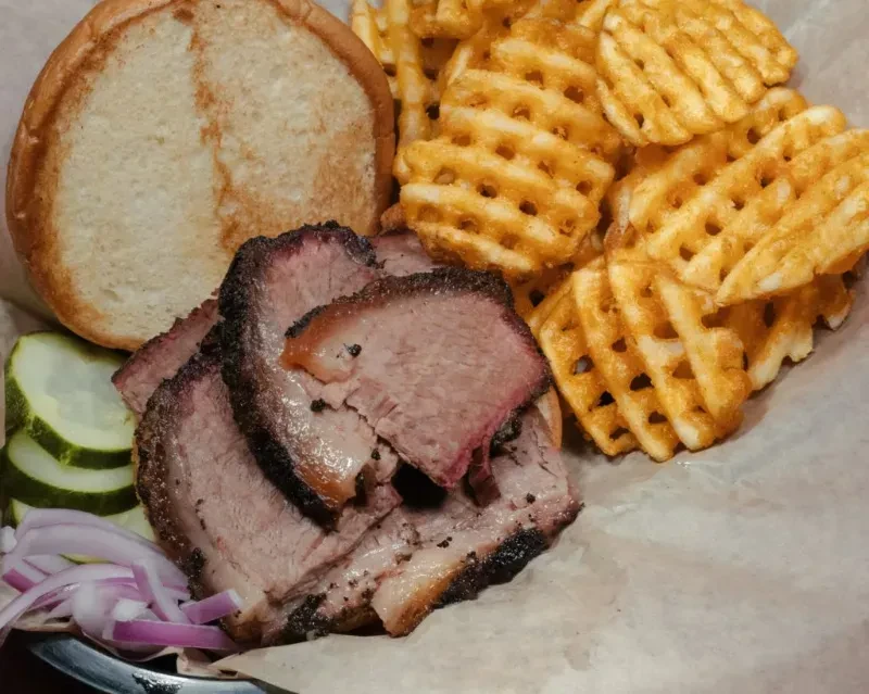 Smoked brisket sandwich with waffle fries, pickles, and red onions.