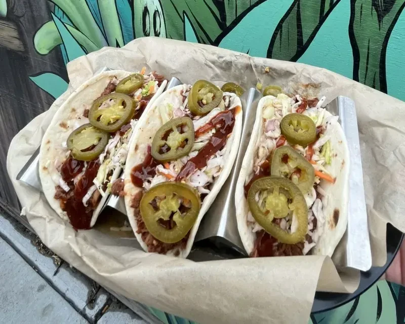 Three tacos with shredded meat, creamy slaw, dark sauce, and jalapeños.