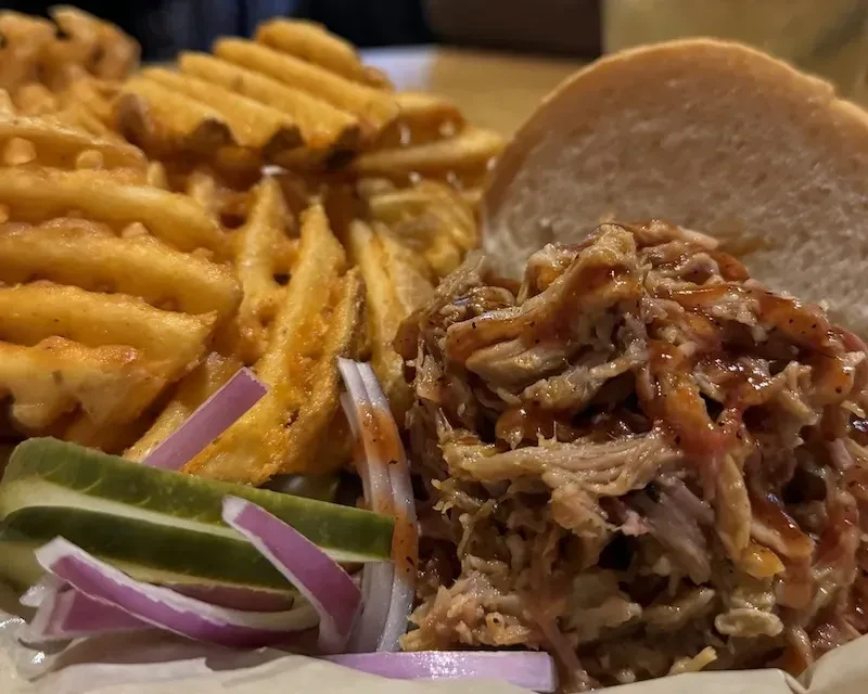 Pulled pork sandwich with waffle fries, pickles, and red onions.