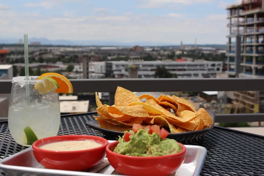 Margarita and appetizers on a rooftop patio overlooking a cityscape.