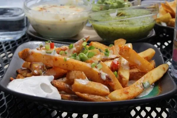 Loaded golden-brown fries with white sauce, green onions, red garnish.