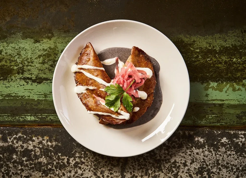 Savory turnover with bean purée, pink onions, cilantro, and white drizzle.