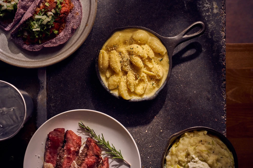 Overhead shot of purple tacos, creamy pasta, steak, and mashed side.